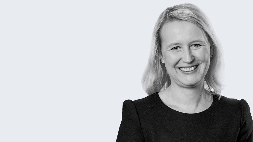 Dr. Anke Dirkmann: Porträt lächelnde, blonde Frau mit schwarzen Oberteil vor grauem Hintergrund (schwarz/weiß Bild).