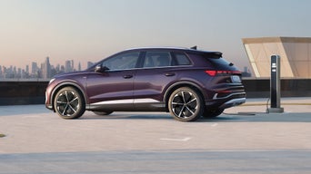 Violetter Audi Q4 e-tron an Ladesäule auf Parkdeck, Skyline im Hintergrund bei Tageslicht, Seitenansicht