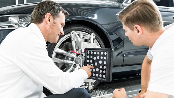 Zwei Männer beugen sich über eine Reifenprüfmaschine an einem Auto.