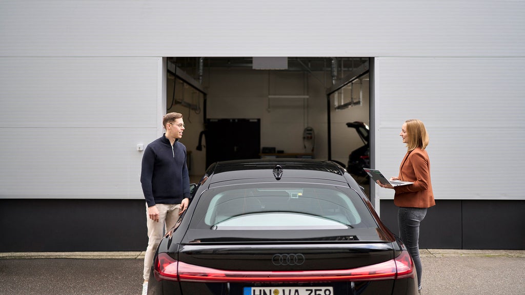Sophia Schupritt is standing opposite her colleague with a laptop in her hand. There is an Audi between them