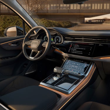 Cockpit eines Audi Q7 SUV TFSI e mit Lederausstattung, Holzdekor, digitalen Anzeigen und zwei Touchscreens in Mittelkonsole.