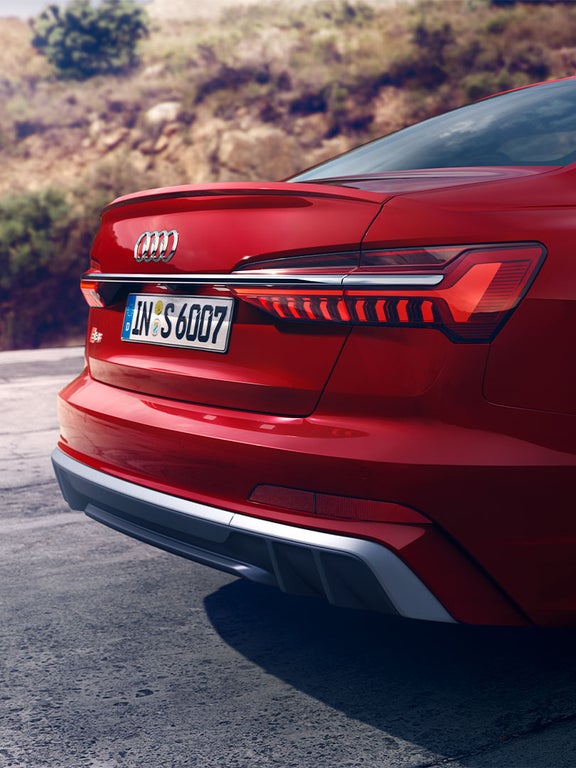 Rückansicht einer roten Audi S6 Limousine TDI mit leuchtenden LED-Rückleuchten und sichtbarem S6-Emblem bei Tageslicht.