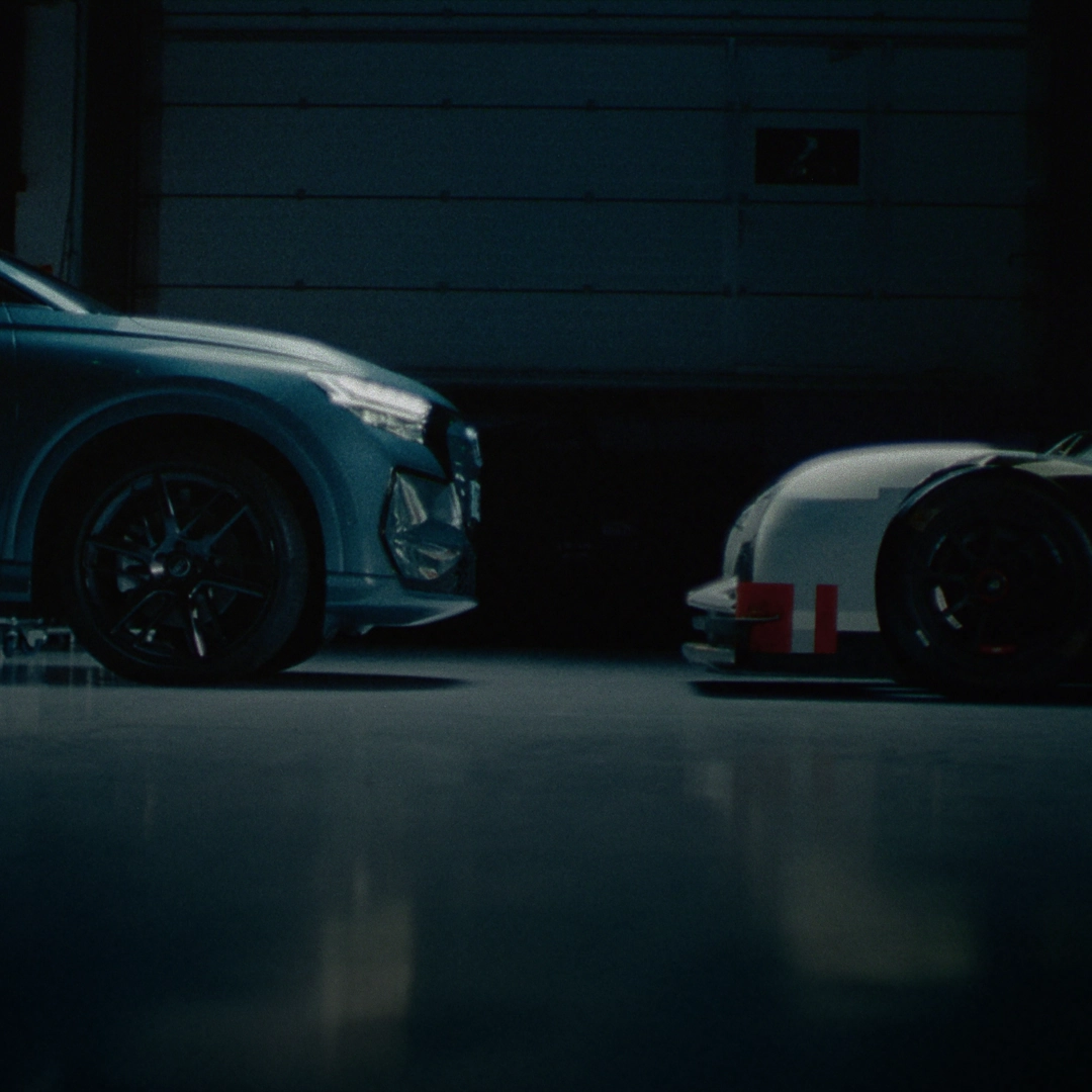 The Q4 SUV e-tron parked face to face with a vintage Audi racing car in a dark garage