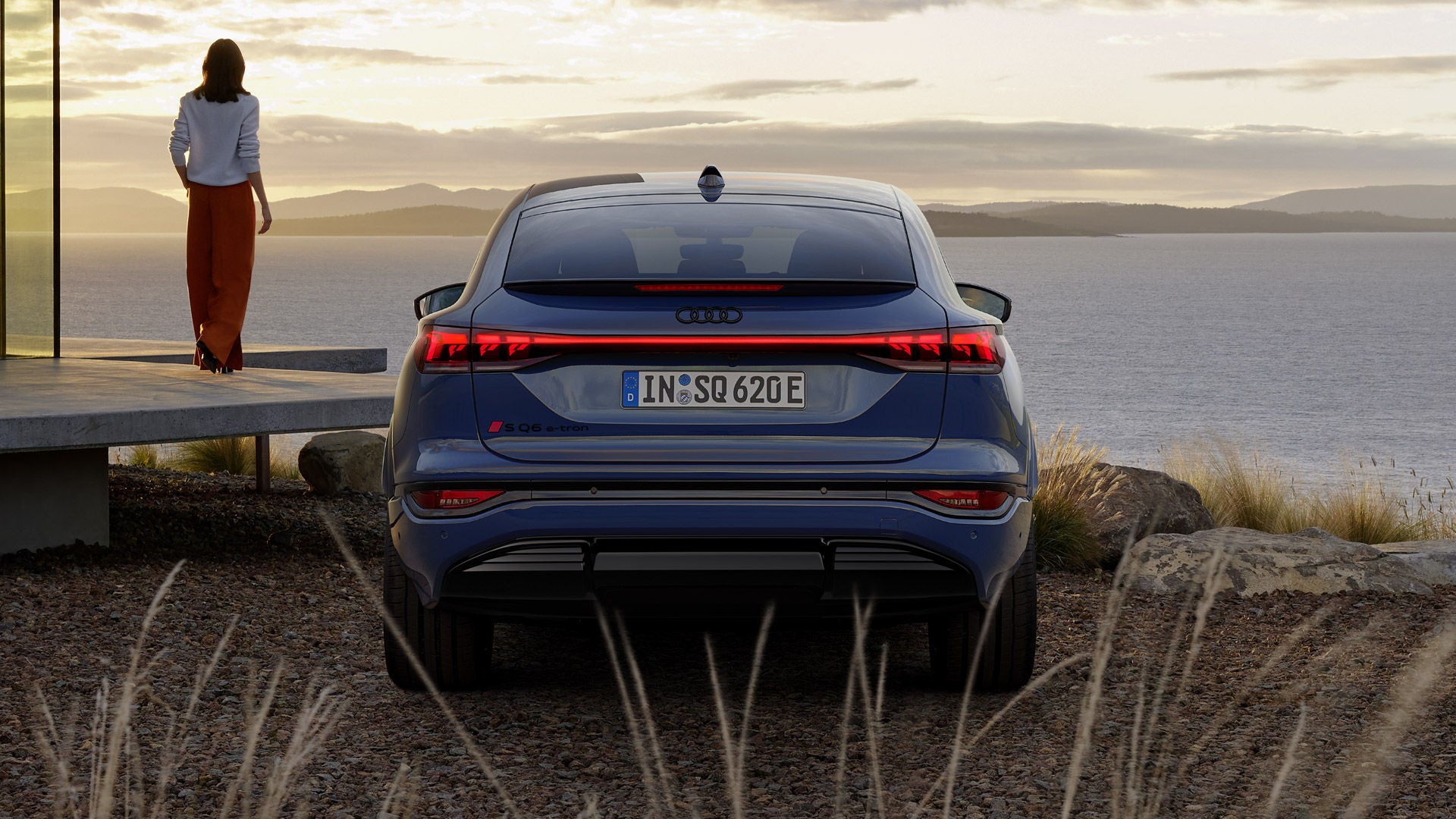 SQ6 Sportback e-tron sedd bakifrån. Till vänster står en person och i bakgrunden syns hav och en solnedgång.