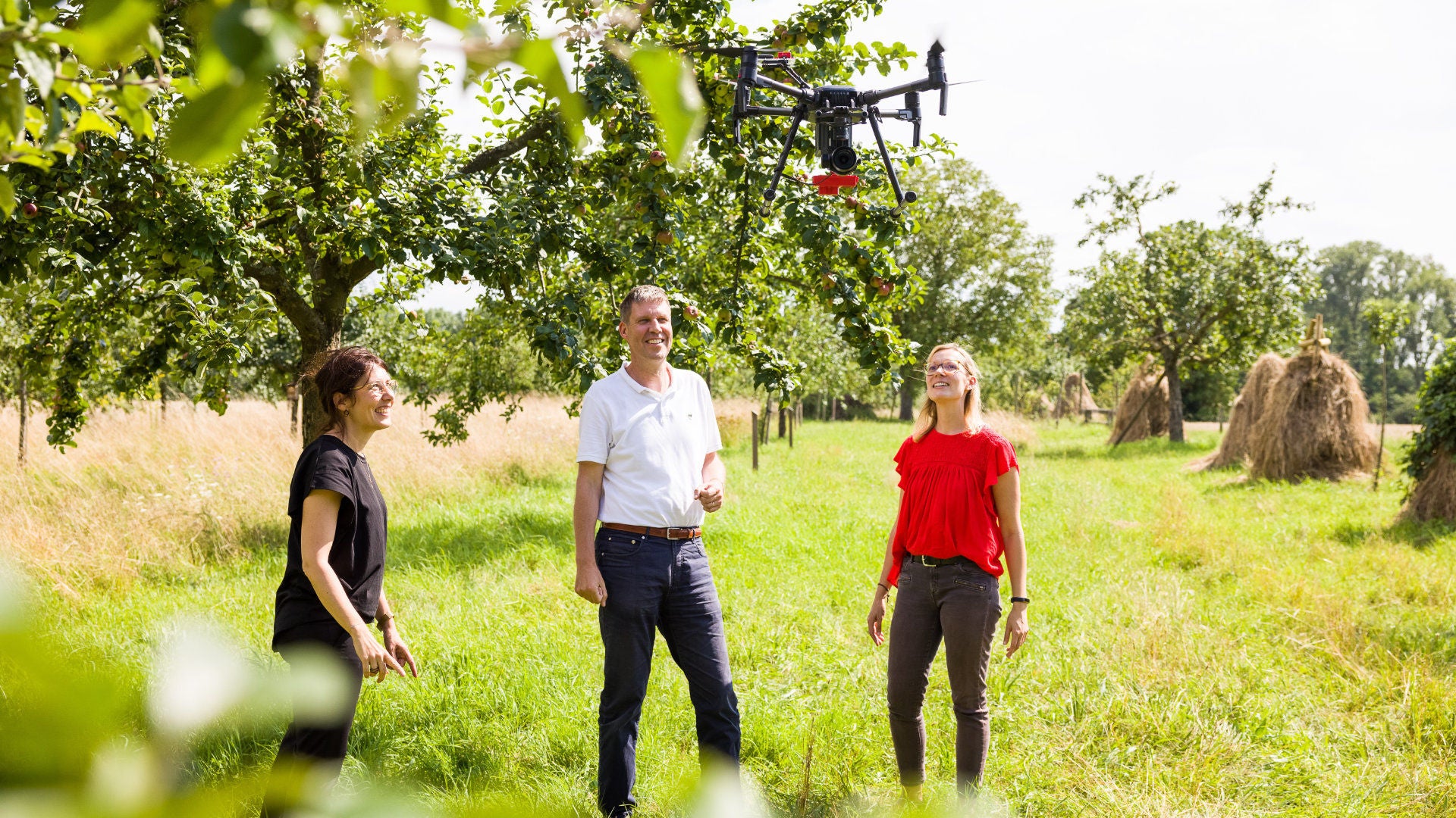 Drei Frauen stehen auf einer Wiese, über ihnen fliegt eine Drohne