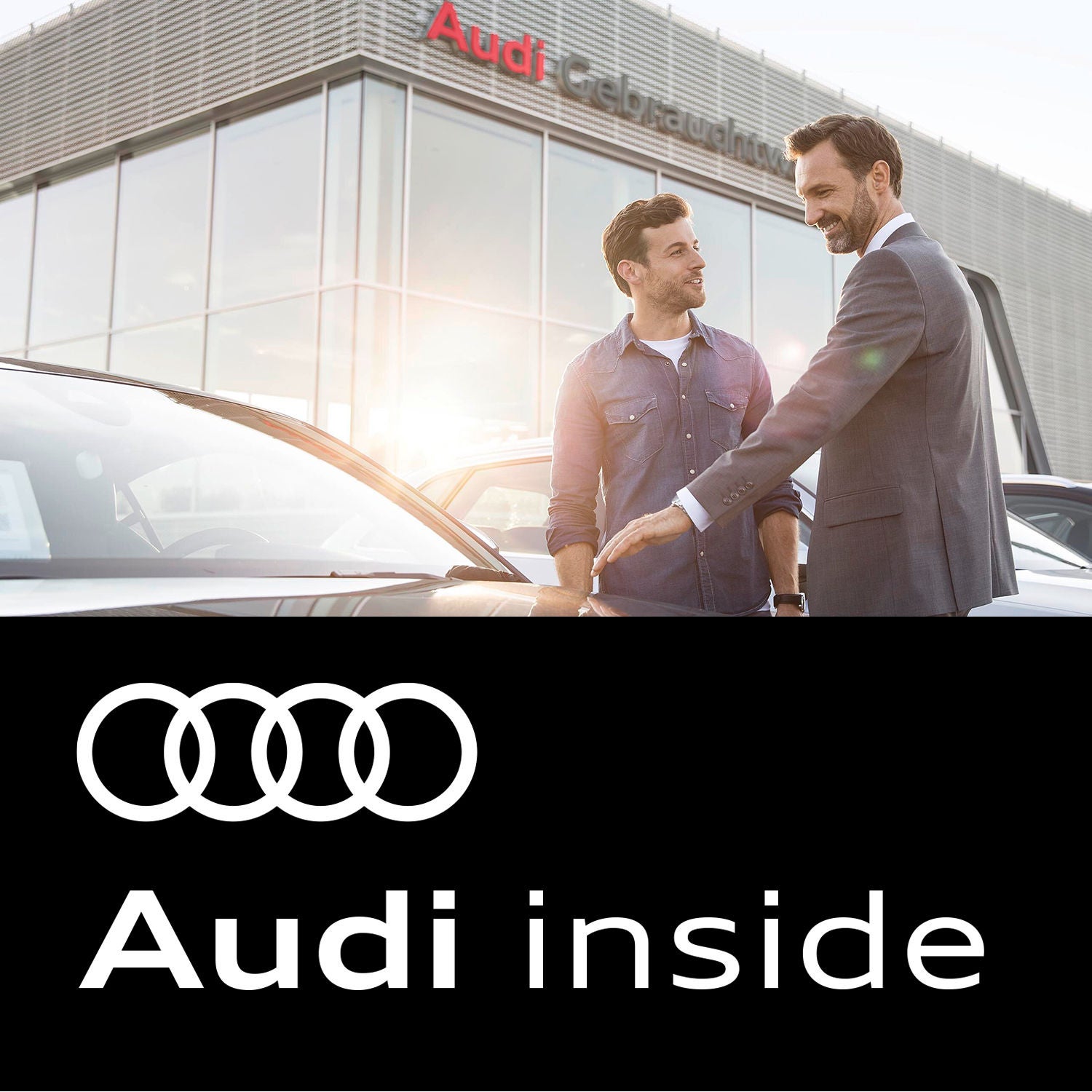 Zwei Männer stehen vor einem Audi-Gebrauchtwagenzentrum und betrachten einen Audi. Darunter sind die vier Ringe von Audi sowie der Schriftzug Audi inside zu sehen