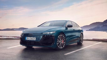 Blauer Audi auf Parkplatz am Meer bei bewölktem Himmel.