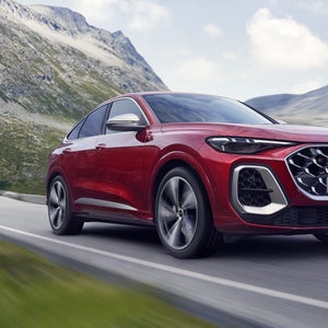Schräges, vorderes Seitenprofil des roten SQ5 Sportback, welcher auf einer Straße durch die Berge fährt.