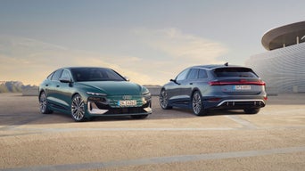 Two sleek Audi cars, a green sedan and a blue SUV, are parked on a concrete surface at dusk. The scene conveys modernity and sophistication.