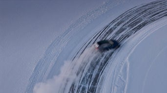 A car drifts on an icy curve; a bird's-eye view of snow spray and tire tracks.