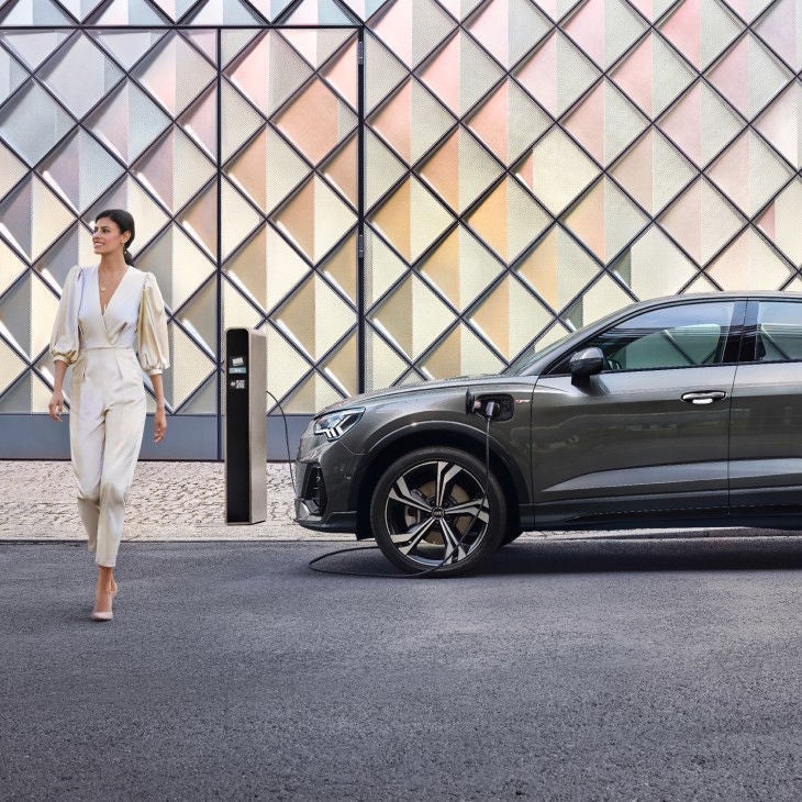 Lady in white walking away from parked dark grey Audi Q3.