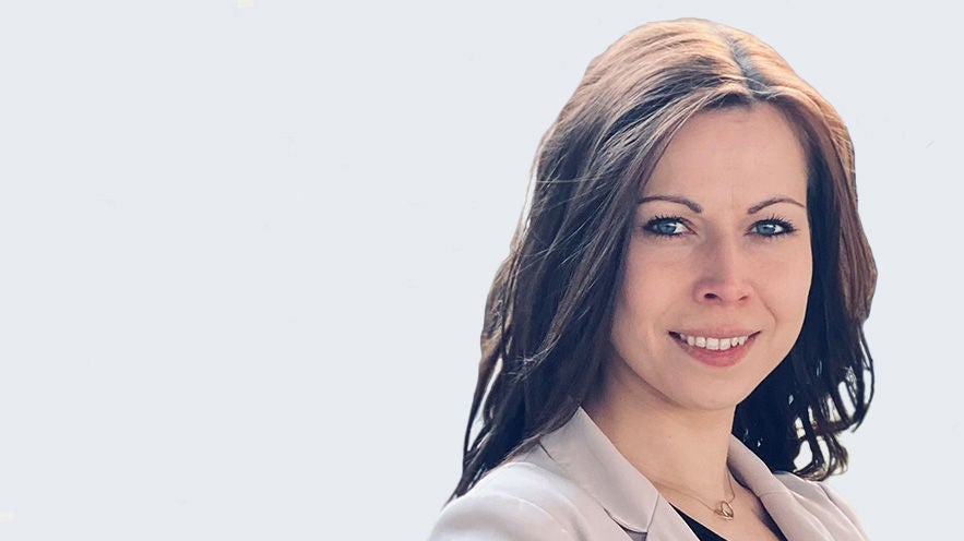 Elisa Elisa: Porträt junge, brünette, lächelnde Frau vor grauem HIntergrund. 