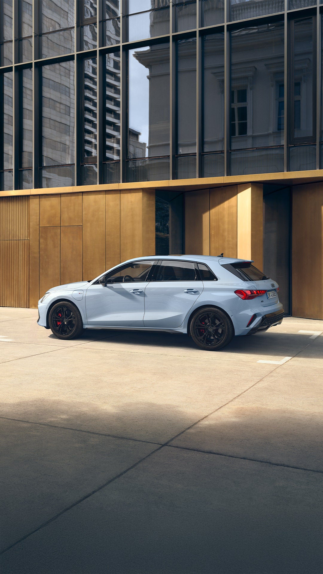 Weißer Audi A3 Sportback TFSI e Seitenansicht auf Parkplatz mit goldfarbener Gebäudefassade im Hintergrund.