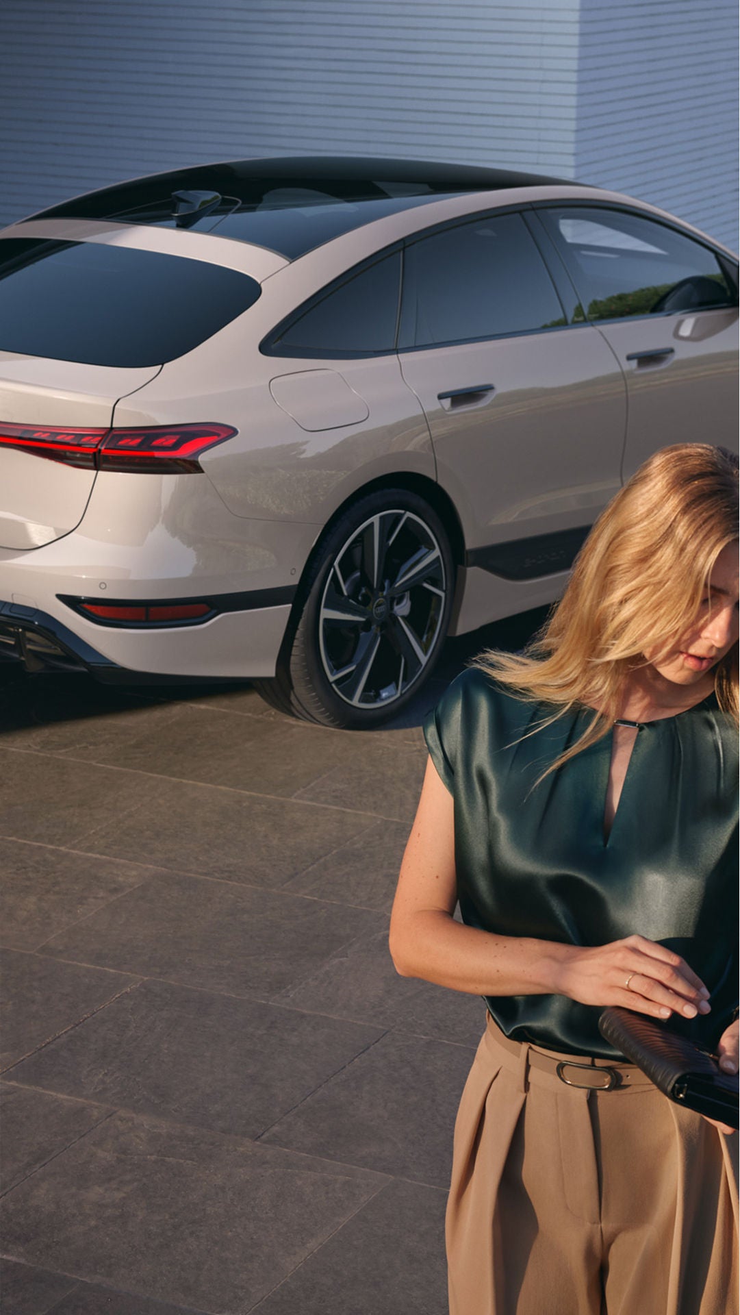 Audi electric sedan with sleek design, parked as a woman stands in elegant, modern surroundings.