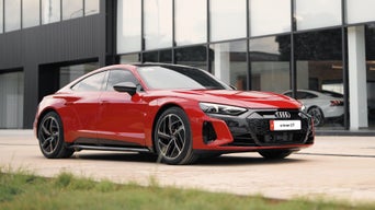 The A6 Sportback e-tron in side profile. The vehicle is parked in the driveway of a building.