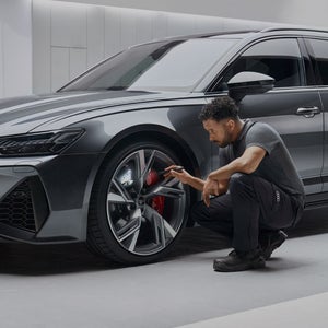 A man squatting down next to an Audi car's wheel