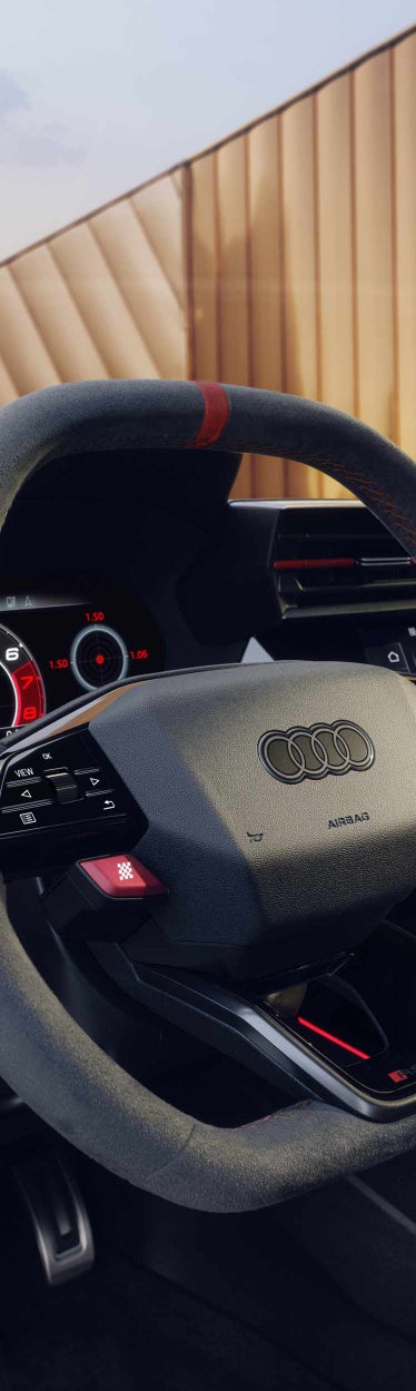 Detailansicht eines Audi-Lenkrads mit roten RS- und Performance-Tasten sowie Alcantara-Bezug mit roter Naht.