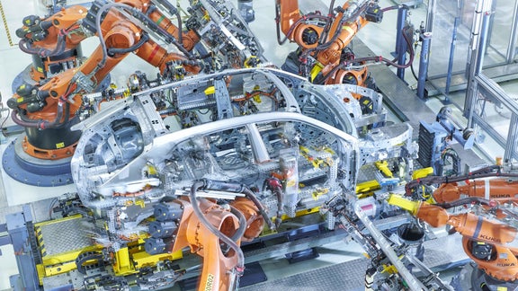 Roboterarme montieren eine silberne Karosserie in einer hochautomatisierten Audi-Fertigungsstraße.
