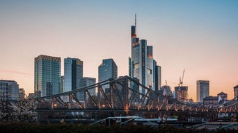 Frankfurter Skyline mit Hochhäusern und Eisenbrücke im Vordergrund bei Sonnenuntergang.