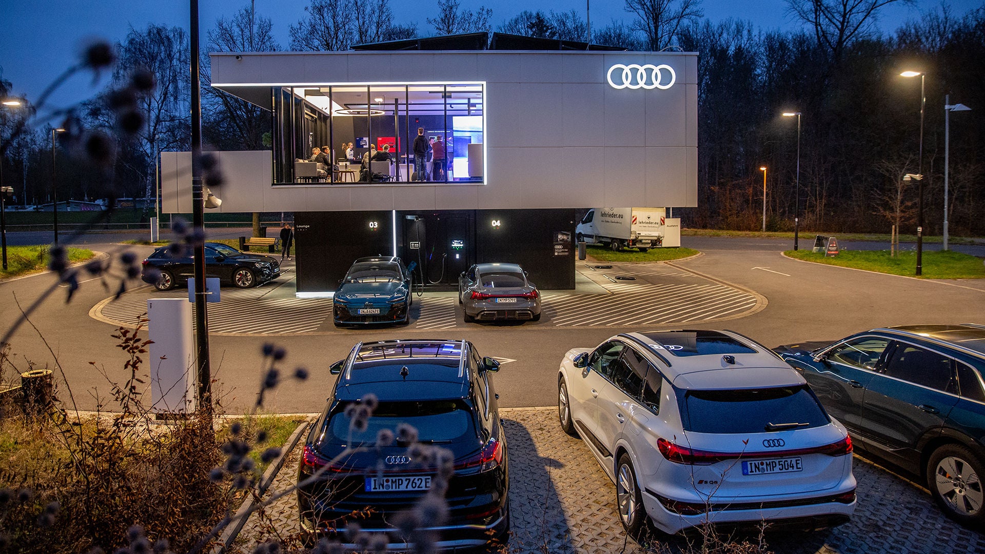 Audi charging hub in Nürnberg im Dunkeln mit einigen Autos vor und Personen im Gebäude