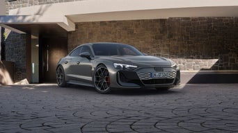 A grey Audi RS e-tron GT parked in front of a modern stone house, showcasing its sporty design and bold front grille.
