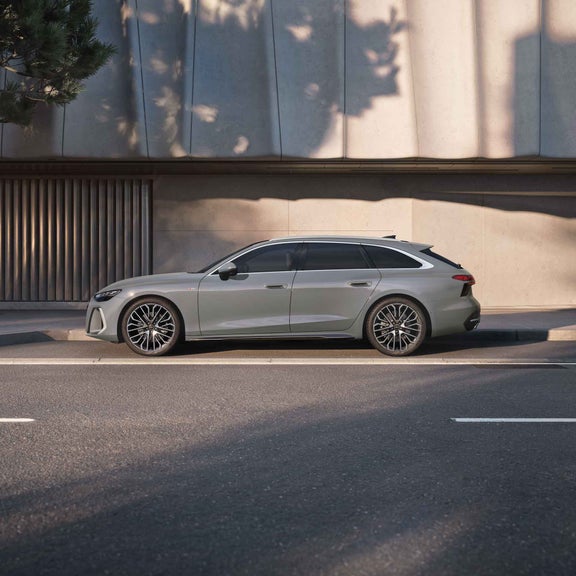 Audi A6 Avant in Quantumgrau steht seitlich vor heller Betonfassade am Straßenrand, moderne Felgen und sportliches Design.
