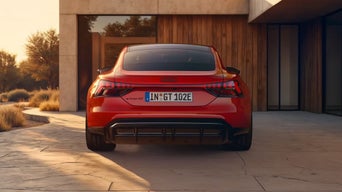 A red Audi e-tron GT parked outside a modern house, showcasing its sleek design and distinctive rear lights at sunset.