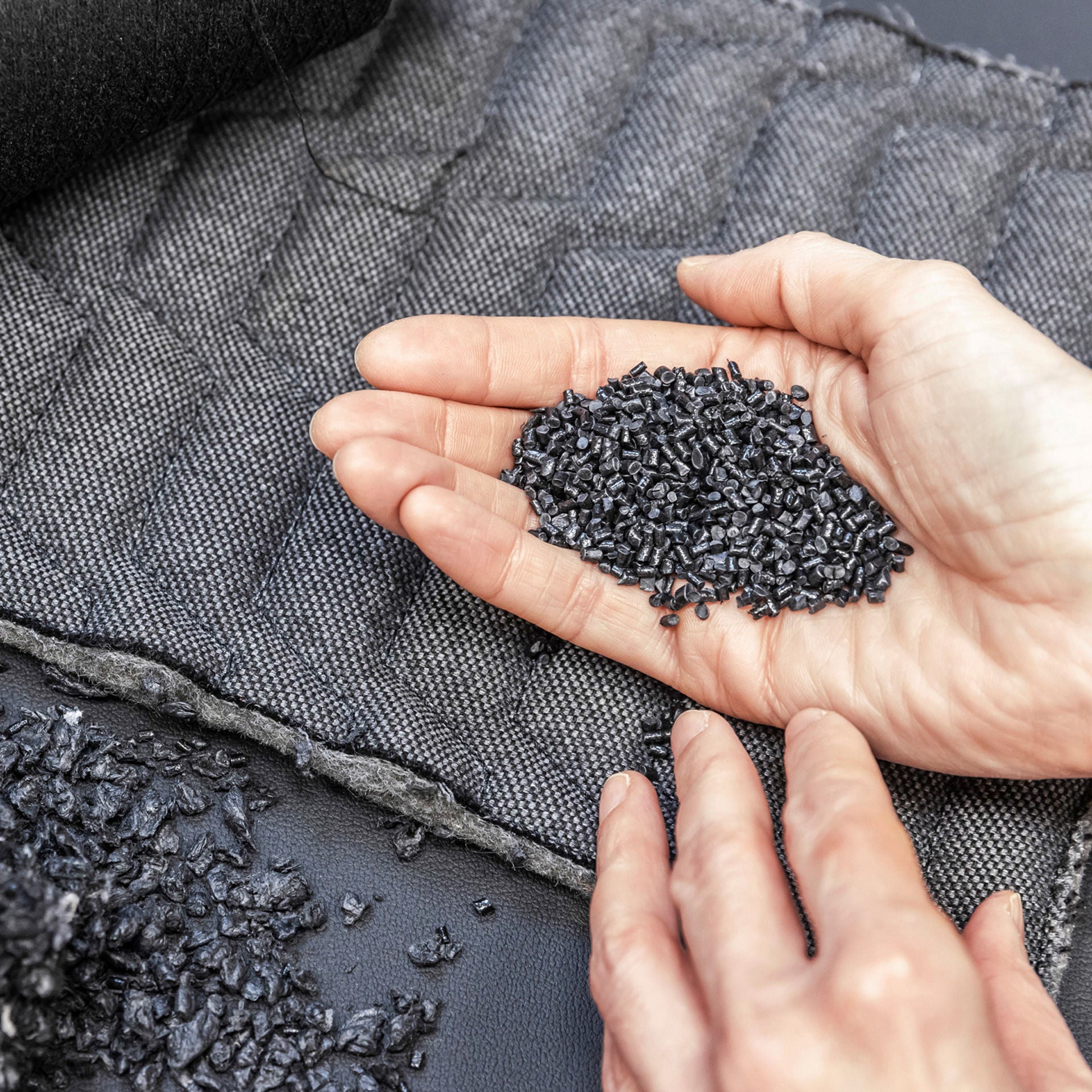 One hand holds a small amount of recyclate