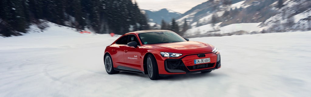 Roter Audi RS e-tron GT performance fährt auf schneebedeckter Strecke durch verschneite Berglandschaft mit Bäumen und Hügeln im Hintergrund.