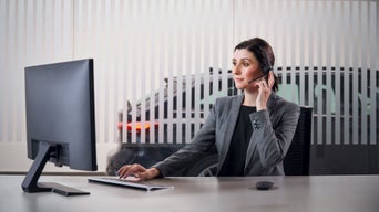 Mitarbeiterin mit Headset sitzt an einem Computerarbeitsplatz und bearbeitet eine Kundenanfrage. Im Hintergrund ist ein Audi Modell zu sehen.