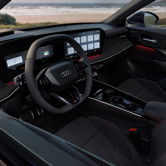 Audi Q3 interior with digital cockpit, touchscreen controls, and red-stitched seats, overlooking a beach.