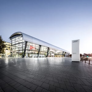 Außenansicht des Audi Forum Neckarsulm mit geschwungener Silberfassade und weißem Markenzeichen-Pylon.