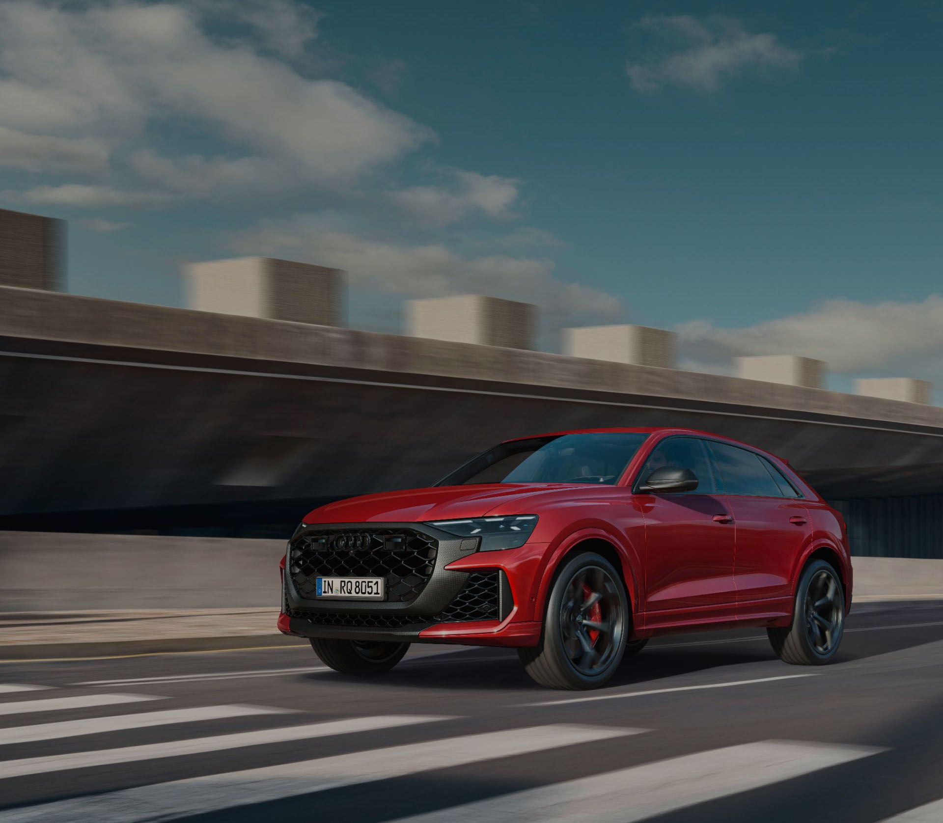 Red Audi SQ8 driven at speed approaching a zebra crossing on a racetrack.