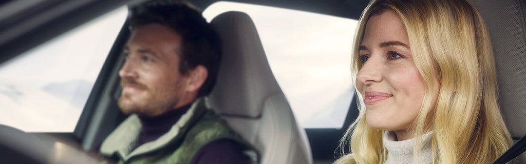 Woman and man sit smiling in a vehicle, with snow and mountains in the background.