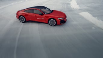 Ein roter Audi fährt auf einer vereisten Teststrecke und driftet durch eine scharfe Kurve, umgeben von Schnee