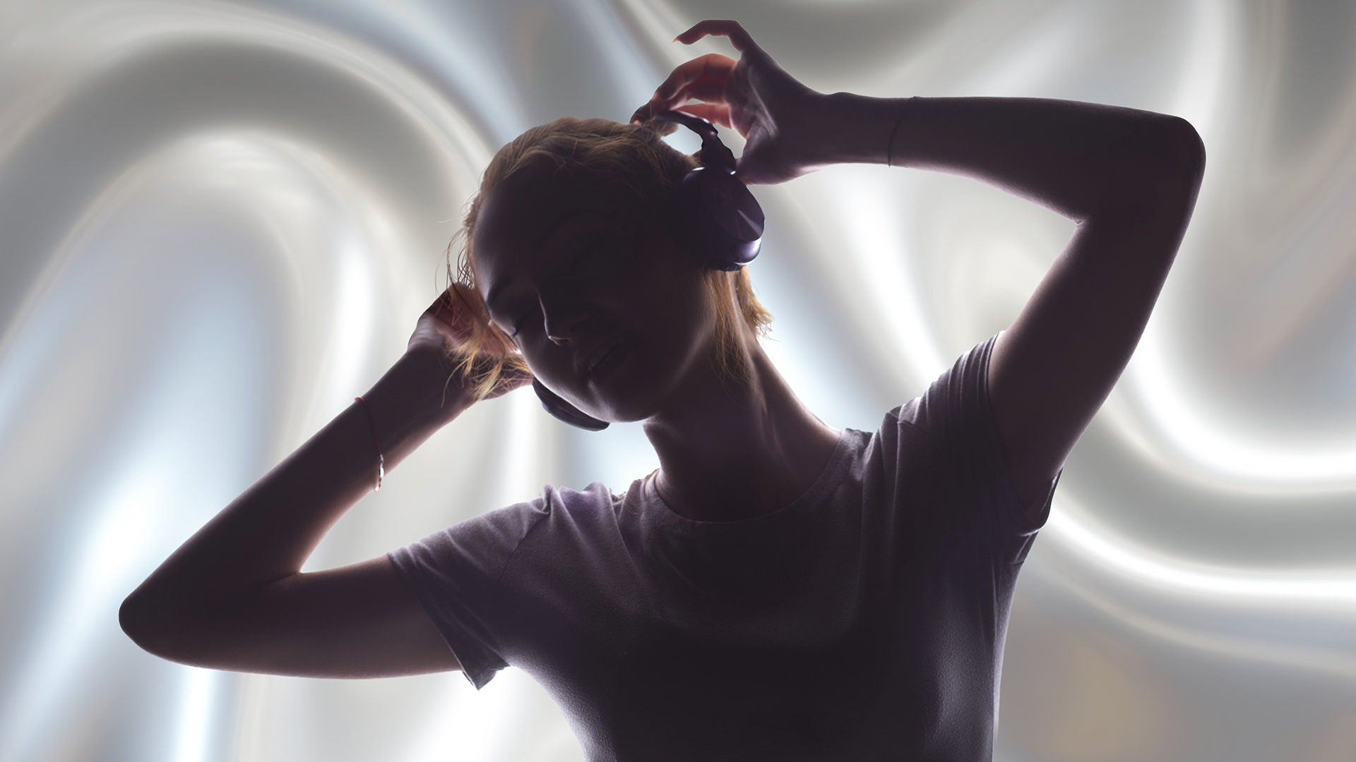 Silhouette einer Frau mit Kopfhörern, Arme über dem Kopf, vor hellem, wirbelndem Licht-Hintergrund.