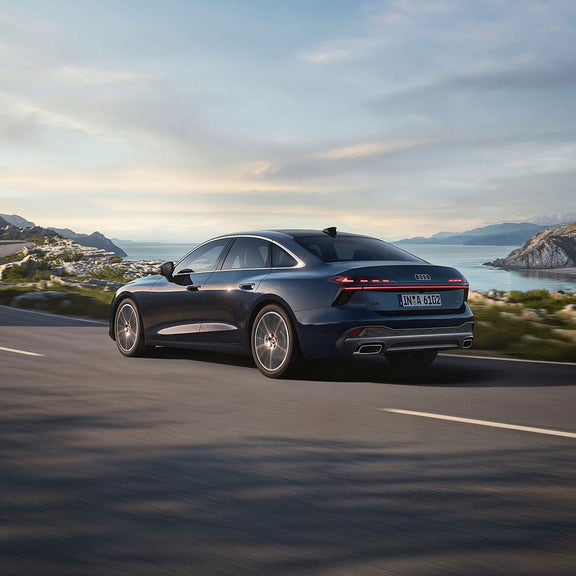 Blue Audi A6 Saloon in motion on curved road with beautiful landscape in the back