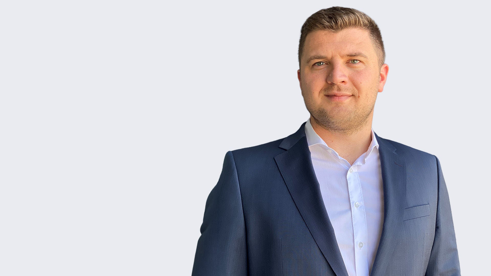 Kushtrim Krasniqi: Mann in blauem Anzug und weißem Hemd vor hellem Hintergrund.