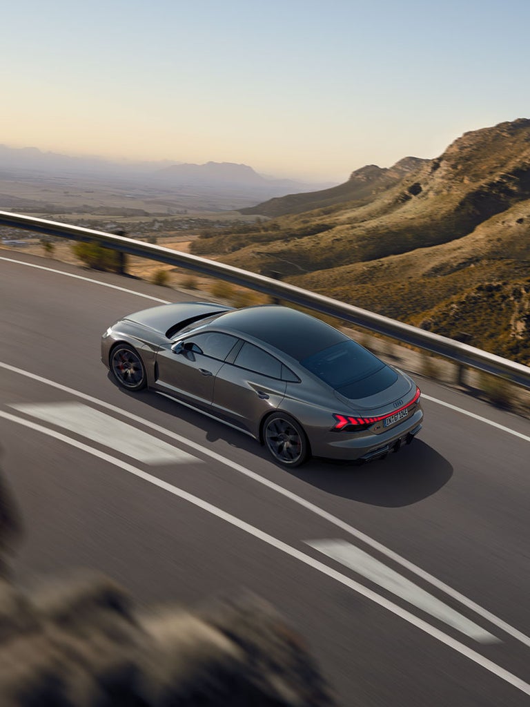 Ein grauer Audi RS e-tron GT fährt auf einer kurvigen Bergstraße mit leuchtenden Rücklichtern.