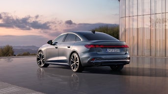 Heckansicht der A5 Limousine, welche vor einem futuristischen Gebäude steht. Im Hintergrund sieht man den Sonnenuntergang an einem leicht bewölkten Himmel.