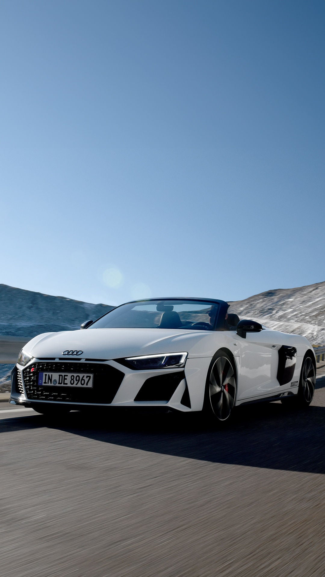 White Audi R8 Spyder V10 performance quattro driving in the mountains in sunny weather with blue skies.