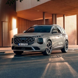 Der neue Audi Q7 in Dreiviertel-Heckansicht fährt auf einer Landstraße in den Sonnenuntergang.