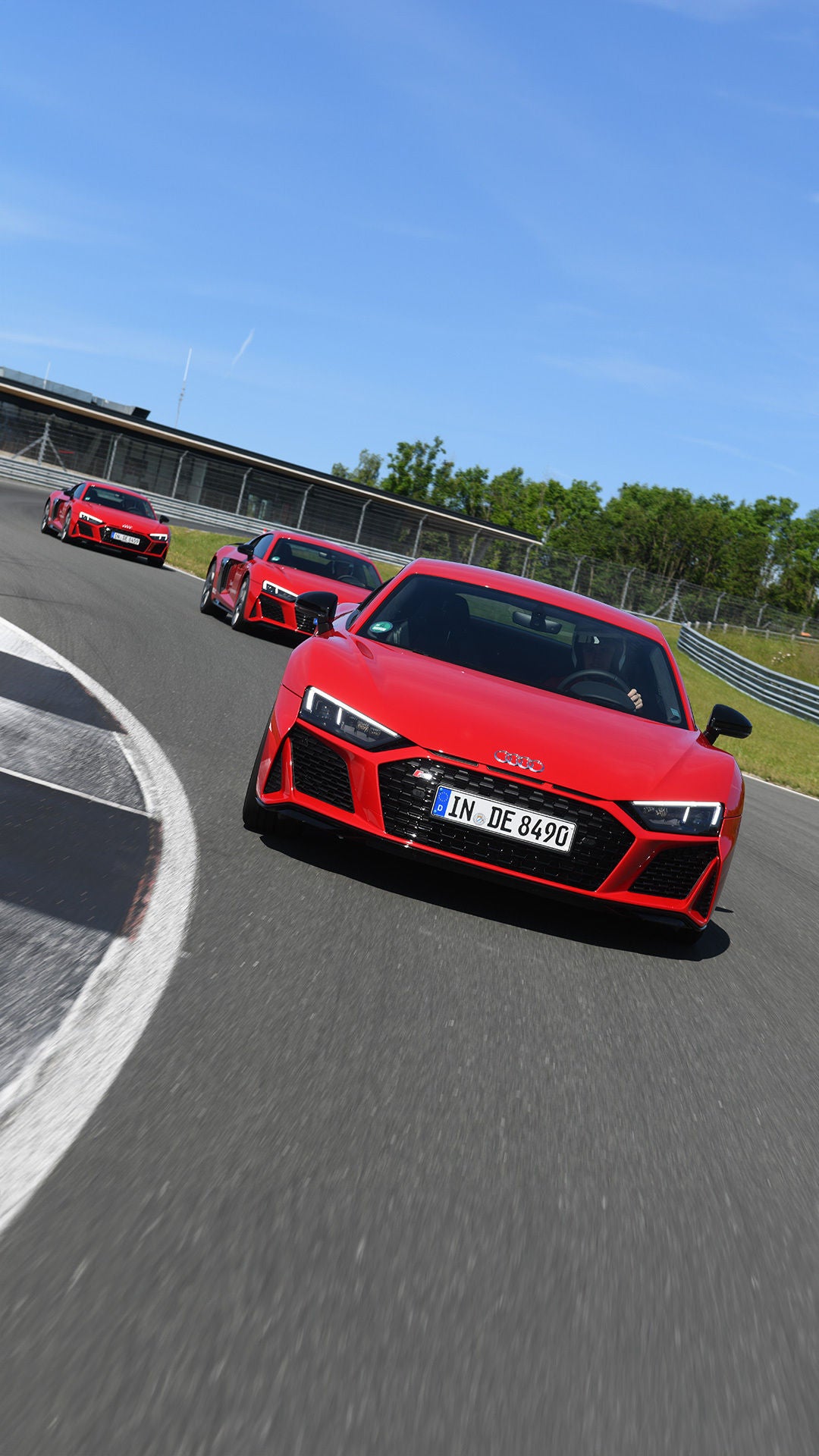 Three red Audi R8 Coupé V10 performance plus models drive head-on behind each other on a race track.