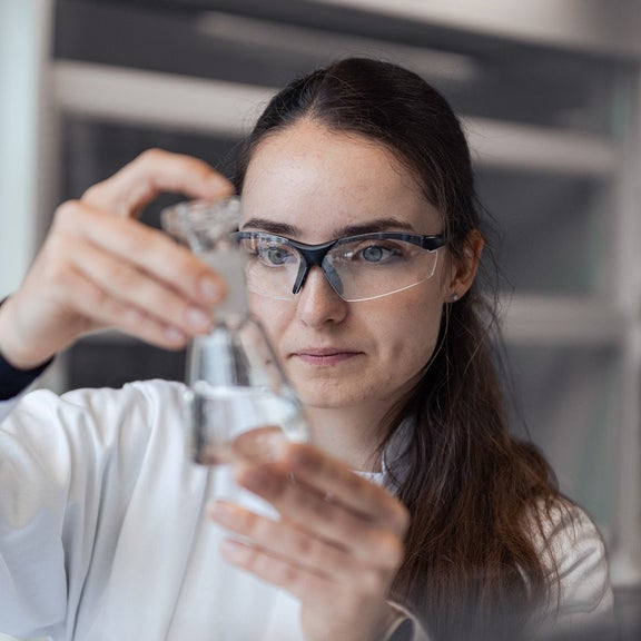 Eine Frau blickt in ein Reangenzglas mit Flüssigkeit.