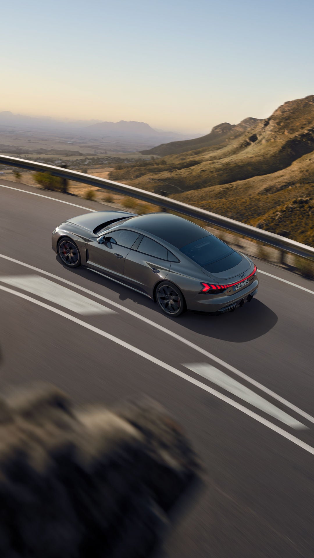 Ein grauer Audi RS e-tron GT fährt auf einer kurvigen Bergstraße mit leuchtenden Rücklichtern.