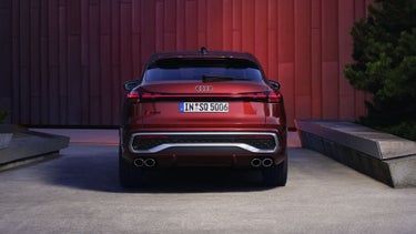 Heckprofil des roten SQ5 Sportback vor einer Gebäudefassade, die vom Fahrzeug rot angeleuchtet wird.