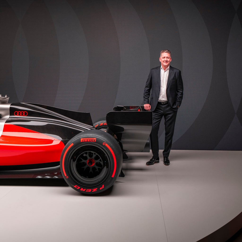 Der Audi Formel-1-Rennwagen R26 mit Rennlakierung in Schwarz, Grau und Rot steht in einem dunklen Studio, daneben steht CEO Gernot Döllner.