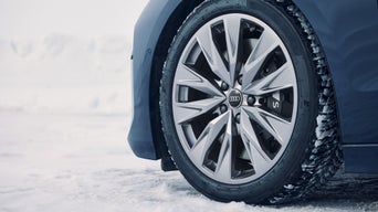 Nahaufnahme des vorderen linken Winterrads eines blauen Audi Modells im Schnee