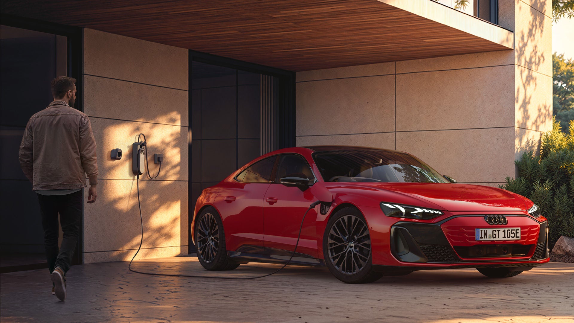 Audi e-tron GT quattro at a charging terminal in front of a modern villa. A casually dressed man is walking toward the car.