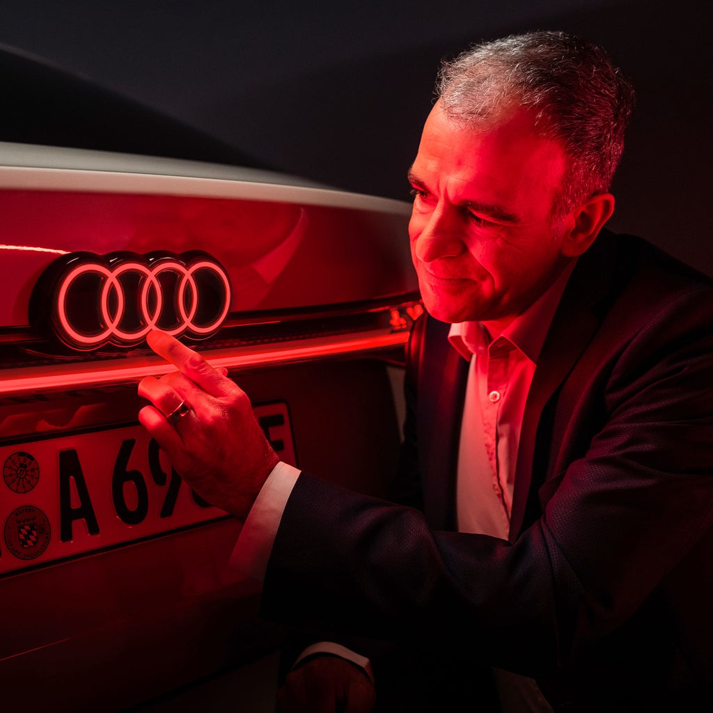 Stefan Staudacher touching the four rings illuminated in red at the back of the Audi A6 e-tron. 